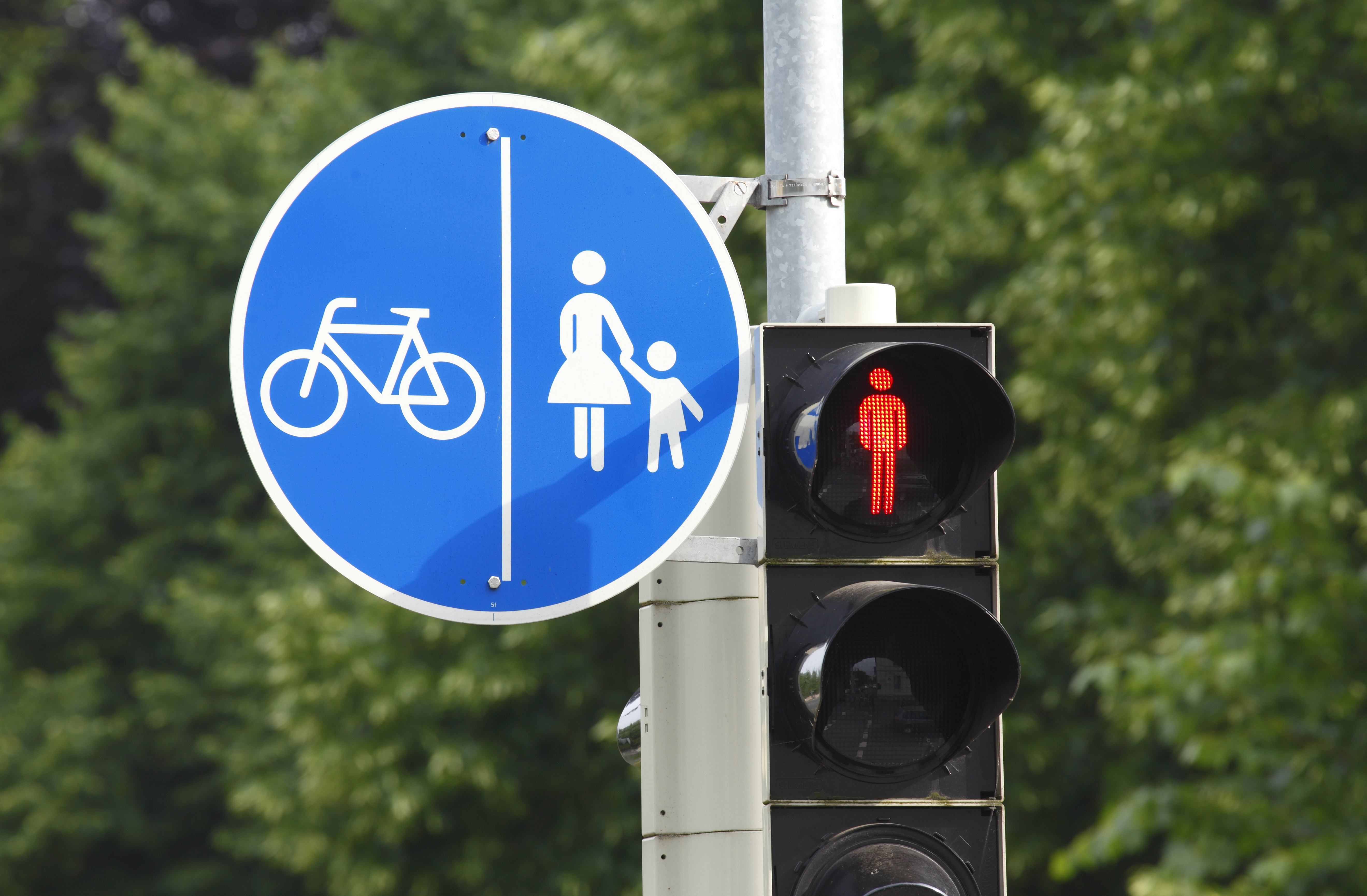 Zu sehen ist ein blaues Verkehrsschild, auf dem Fußgänger und ein Fahrrad abgebildet sind, die durch eine vertikale Linie getrennt werden.